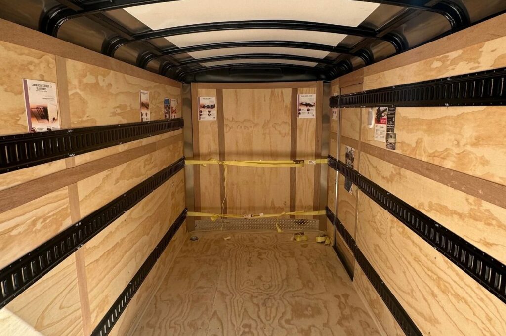 Empty cargo trailer interior with plywood walls and tie-down rails.
