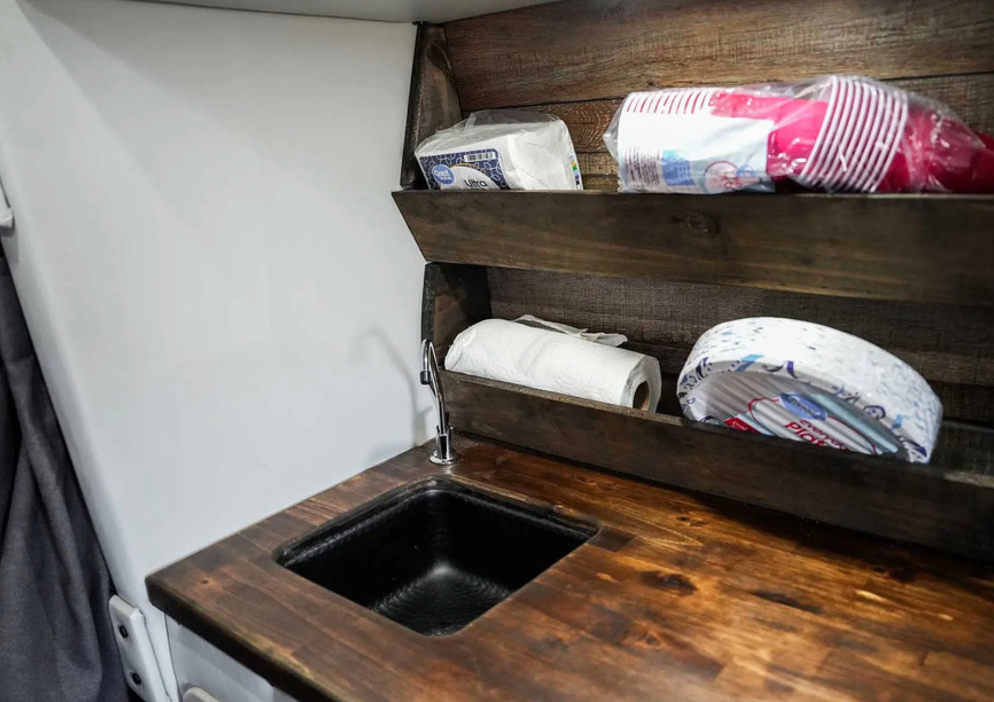Wooden camper van kitchenette counter with sink and shelves.